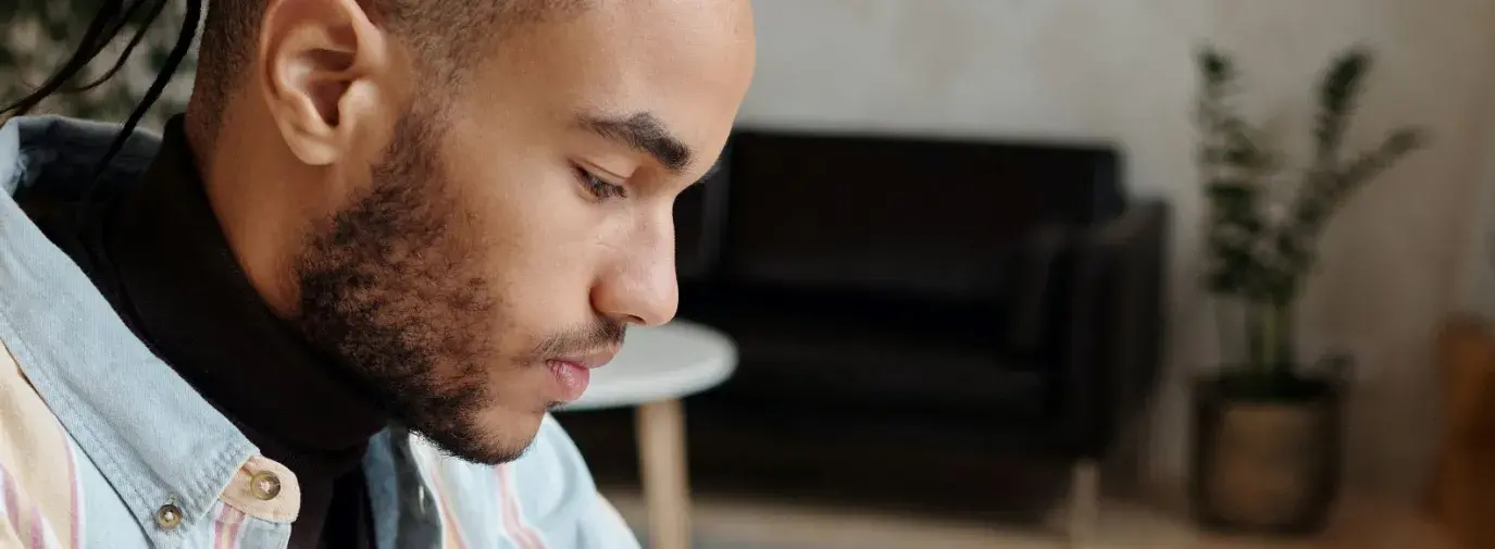 young black man wearing a flannel and studying or working at a desk with a notebook and a cup of coffee.